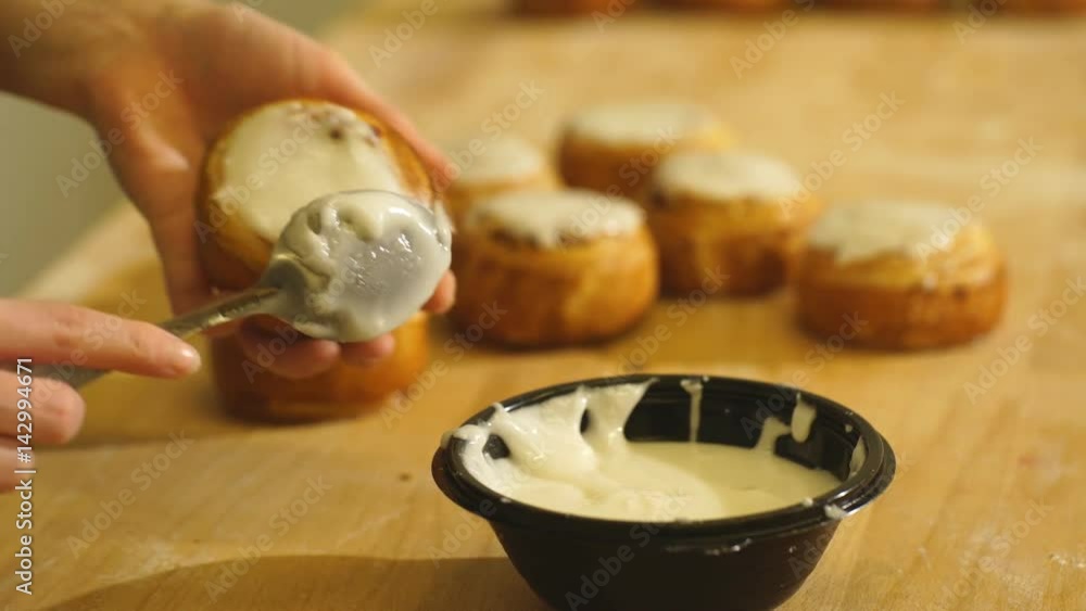 Woman's Hand Spreading Frosting Across Freshly Baked Cinnamon Rolls Woman's Hand Spreading Frosting Across Freshly Baked Cinnamon Rolls