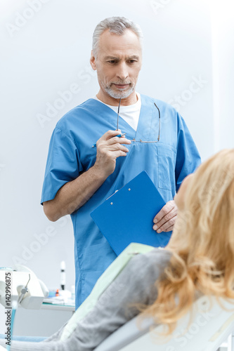 senior dentist in uniform talking with patient in dental clinic