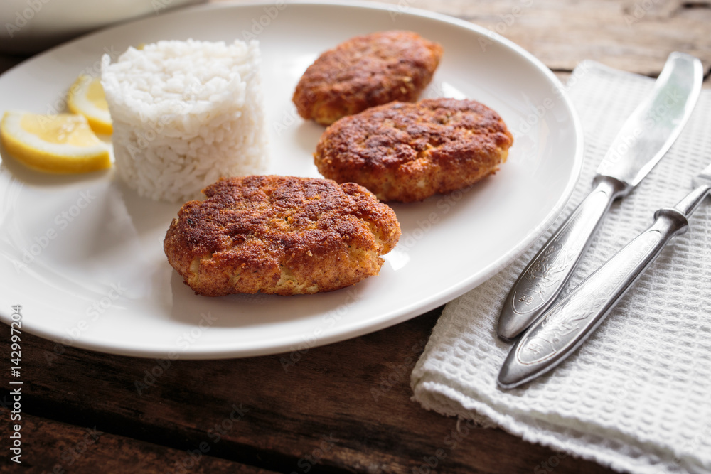 Three croquettes on white ceramic plate with cutlery aside on wooden table Three croquettes on white ceramic plate with cutlery aside on wooden table