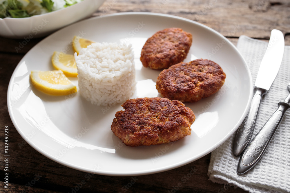 Three fish breadcrumbed cutlet on white plate with rice. Restaurant menu background