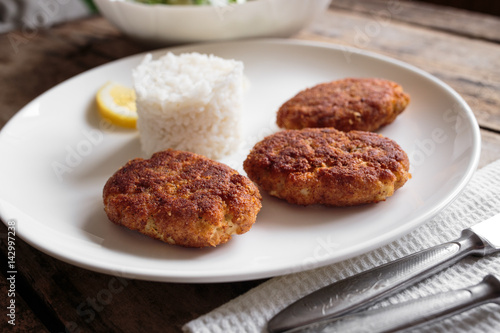 Three fish breadcrumbed cutlet on white plate with rice. Restaurant menu background