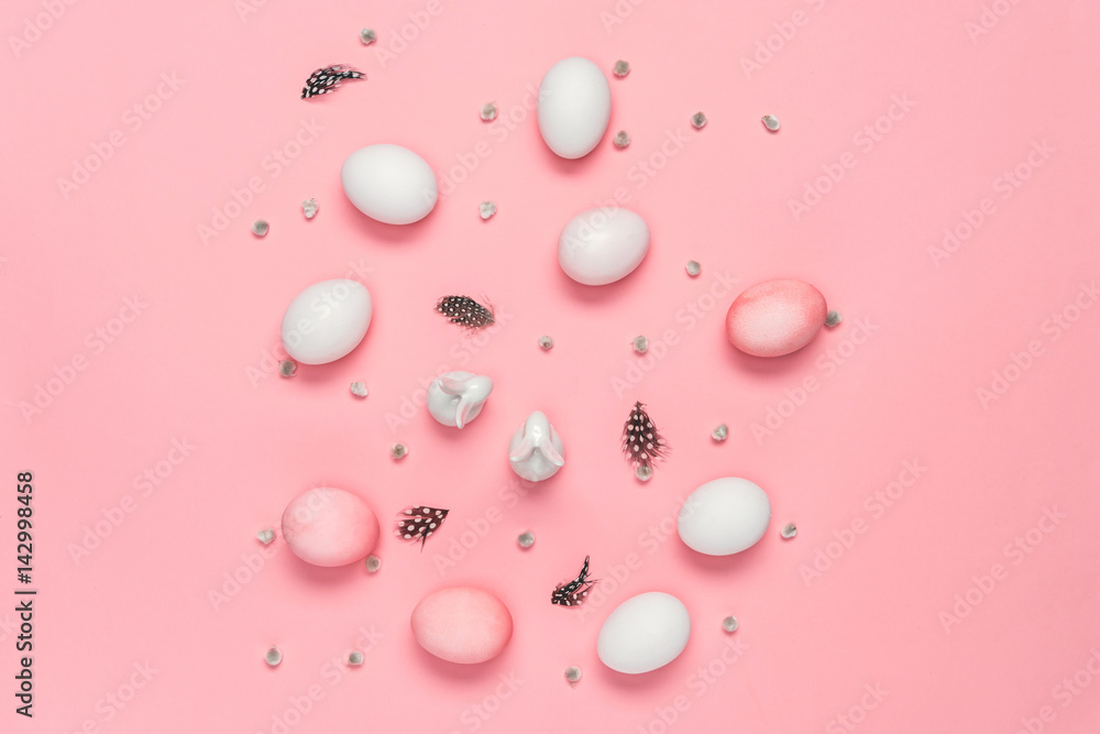 Top view of pink and white eggs with bunnies, catkins and feathers on pink. Happy Easter concept