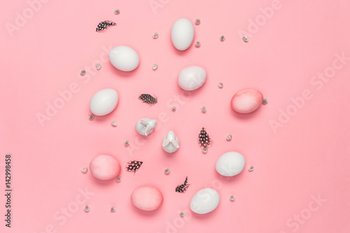 Top view of pink and white eggs with bunnies, catkins and feathers on pink. Happy Easter concept