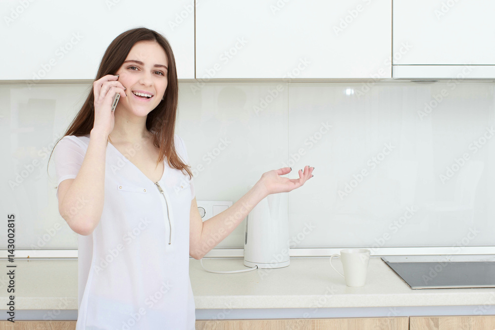 Brunette housewife in white in the kitchen talking on the mobile phone Brunette housewife in white in the kitchen talking on the mobile phone