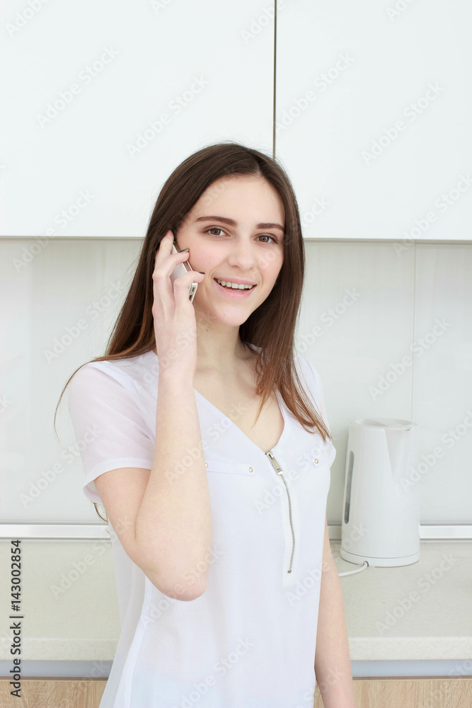Brunette housewife in white in the kitchen talking on the mobile phone Brunette housewife in white in the kitchen talking on the mobile phone