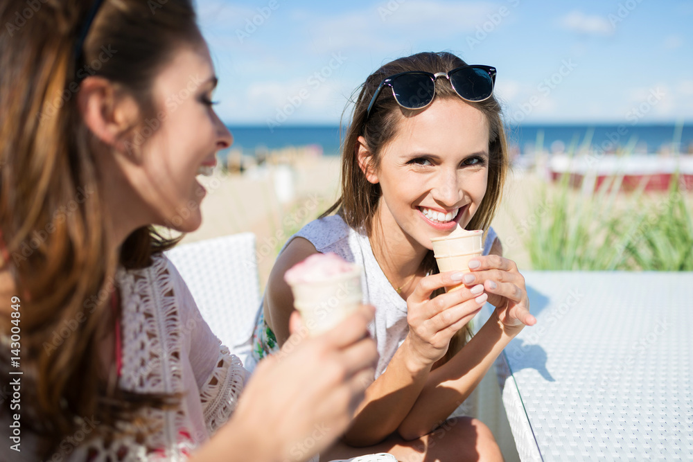 Beautiful woman eating ice cream outside with her friend laughing Beautiful woman eating ice cream outside with her friend laughing