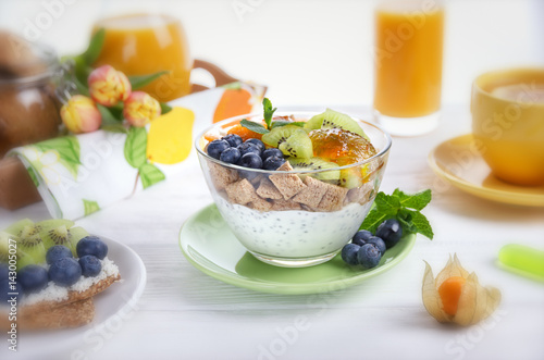 Breakfast. Yogurt with chia seeds  corn pads  kiwi  blueberries and physalis. Lemon tea  juice and toast with fruit on a blurred background. Selective focus.