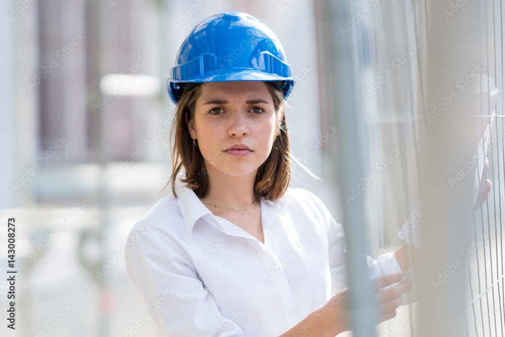 Absorbed female engineer wearing blue helmet among scaffolding. Selective focus Absorbed female engineer wearing blue helmet among scaffolding. Selective focus