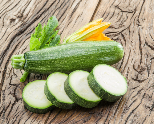 Zucchini with slices and zucchini flowers on a wooden table.