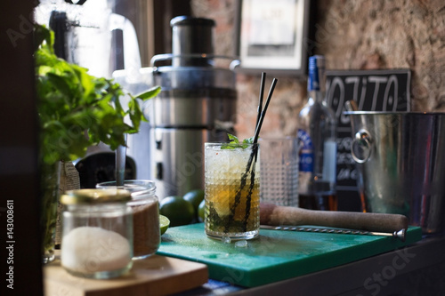 A fresh and juicy mojito with rum crushed ice mint and lemon stands on a working surface in a trendy bar in downtown