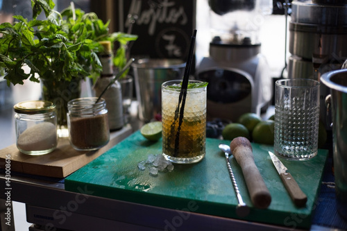 A selective focus shot of refreshing summer mojito in the messy and full of character bar in downtown with muddler and mixer on the cutting board