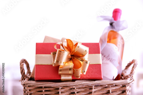 Wine bottle with gift boxes in wicker basket on light background