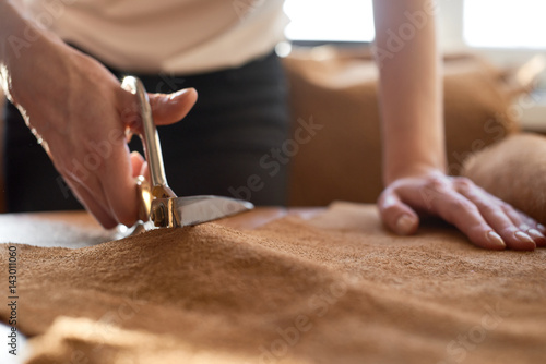 Female artisan cutting brown leather with scissors close up photo