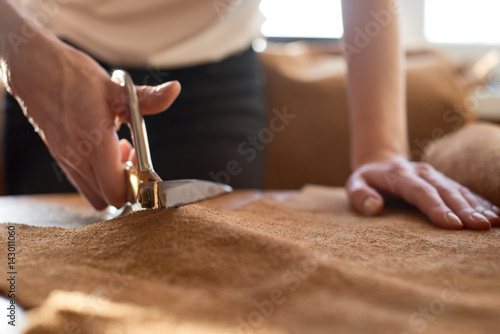 Картината върху платно Female artisan cutting brown leather with scissors close up