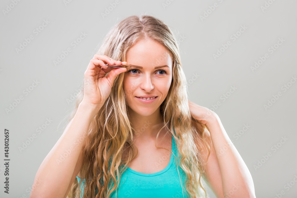 Beautiful young woman plucking eyebrows on gray background. Beautiful young woman plucking eyebrows on gray background.