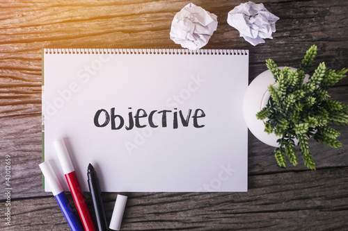 Objective word with Notepad and green plant on wooden background.