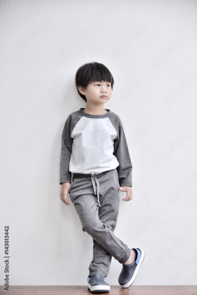 Little boy looking away and standing against white wall Little boy looking away and standing against white wall