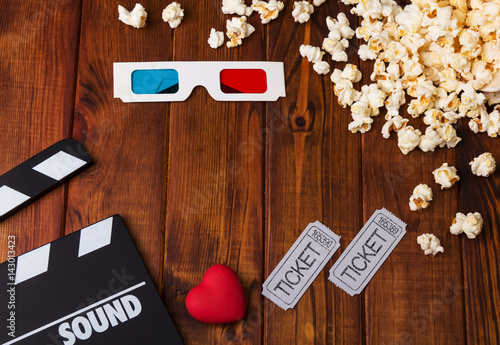 3D-glasses, popcorn, red heart, movie tickets and movie clapper against dark wood.