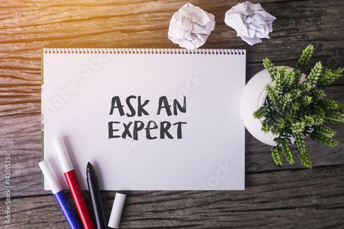 Ask An Expert word with Notepad and green plant on wooden background.