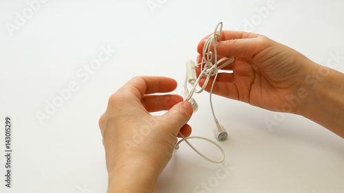 Woman untangling tangled earbuds or earphone knot with hands photo