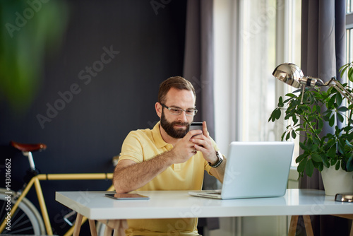 Young entrepreneur using smart phone while sitting in his personal home office