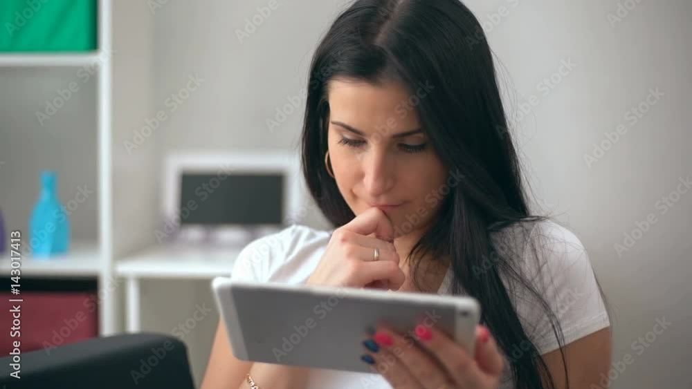 Brunette women using a tablet pc sitting on the sofa in a living room Brunette women using a tablet pc sitting on the sofa in a living room