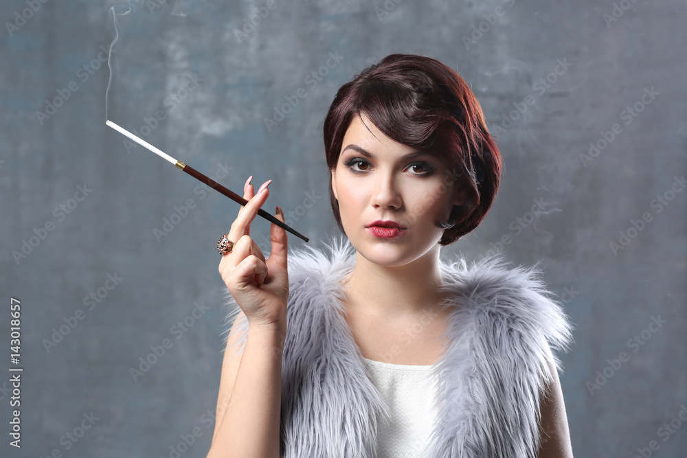 Obraz premium Young woman smoking with cigarette holder on color background