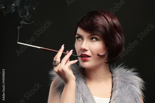 Young woman smoking with cigarette holder on dark background