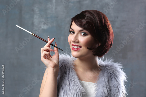 Tableau sur toile Young woman with cigarette holder on color background
