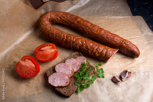Slices of smoked sausage with spice, herbs and vegetables on the packaging paper.
