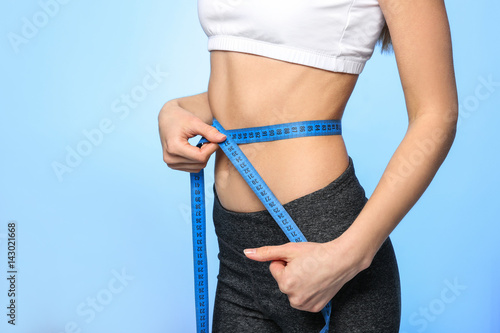 Diet concept. Young woman with measuring tape on light background