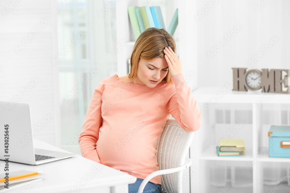 Pregnant woman suffering from headaches while sitting at workplace in office Pregnant woman suffering from headaches while sitting at workplace in office