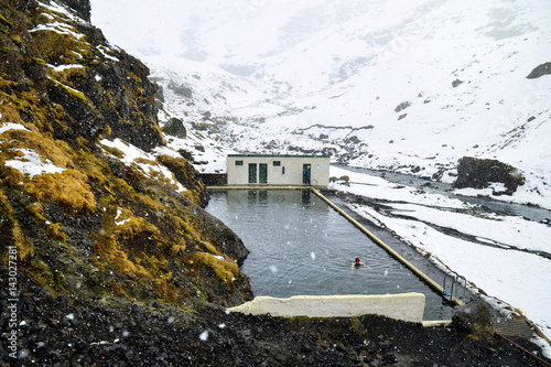 Natural swimming pool Seljavallalaug in iceland with man in water and snowy weather and mountains all around