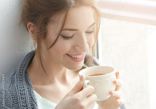 Valokuva Beautiful young woman drinking tea near window at home