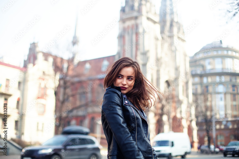 Fototapeta premium young beautiful brunette walking the city.leather jacket,urban backpack , bright red lips The concept of street fashion.
