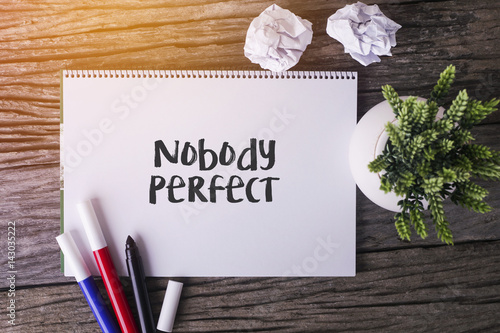 Nobody Perfect word with Notepad and green plant on wooden background.