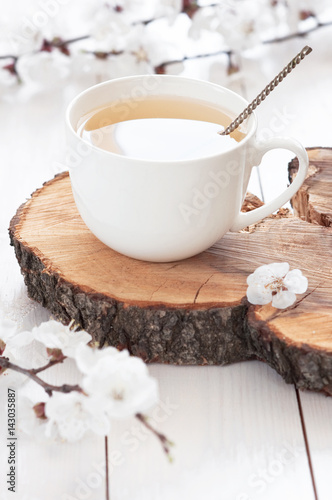 White cup of hot tea with spring flowers on a light wooden background
