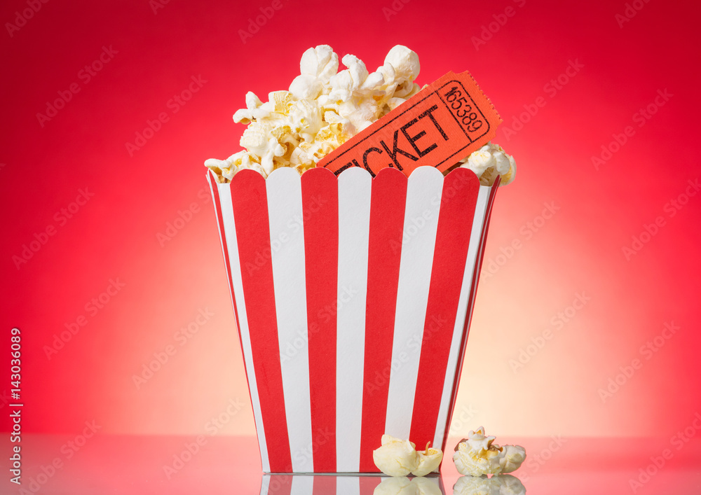 Large square box with popcorn and movie tickets on bright red .