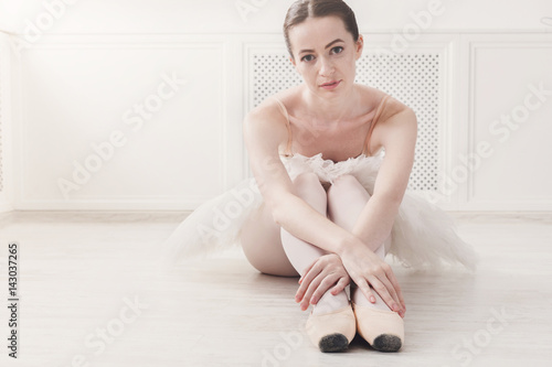 Closeup of young ballerina sit in pointe shoes on white floor background
