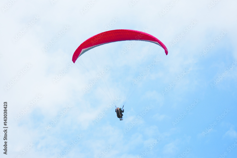 One paraglider in the blue sky with red parachute gliding for fun and excitement towards the ground. One paraglider in the blue sky with red parachute gliding for fun and excitement towards the ground.