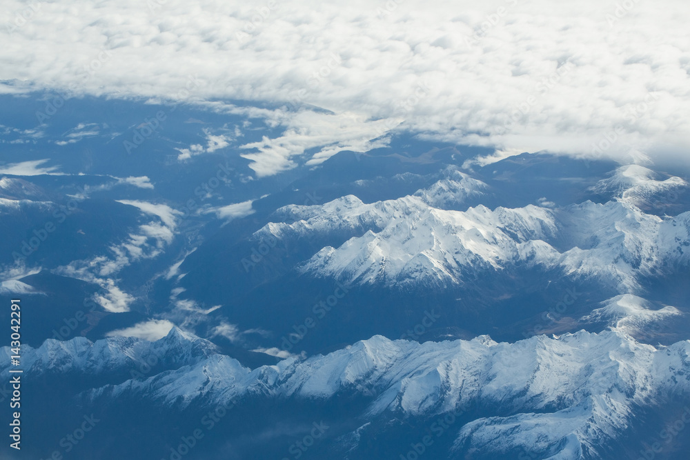 Obraz premium Idyllic snowy mountain peaks under clouds from plane