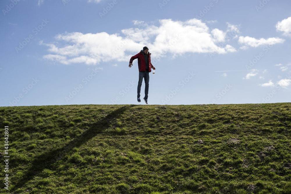 Mann auf einem Deich springt und macht faxen vor blauem Himmel Mann auf einem Deich springt und macht faxen vor blauem Himmel