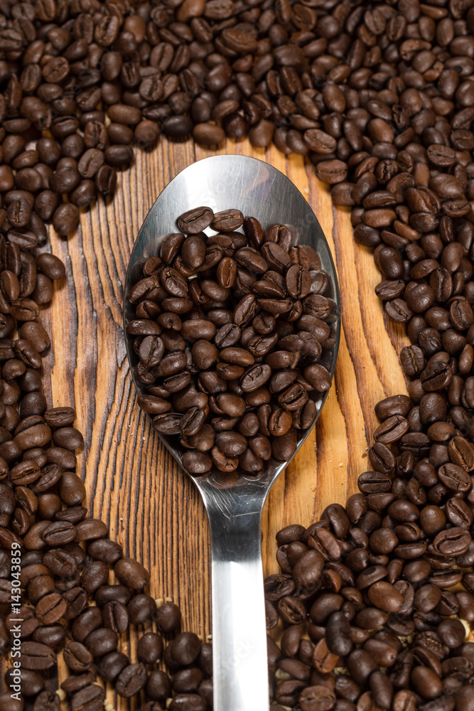 Fototapeta premium Aromatic goodness. A spoon full of roasted coffee beans surrounded by coffee beans scattered on the table...
