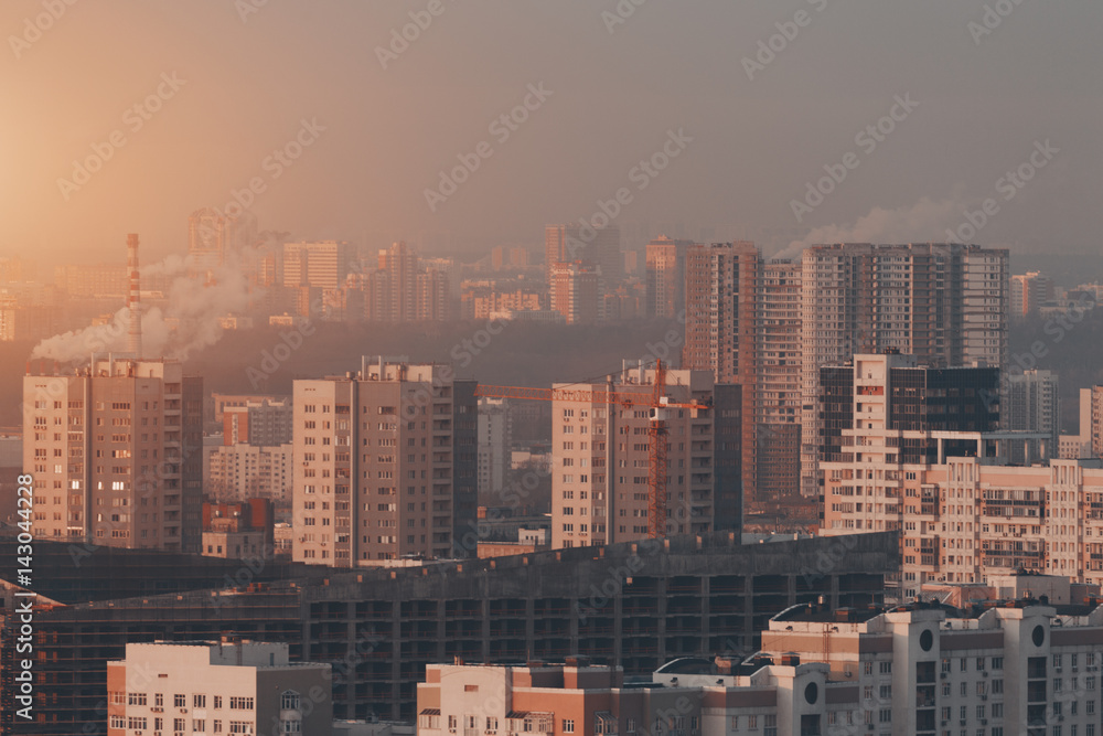 Fototapeta premium Close-up shooting from top of morning metropolitan city with grey unfinished residential or office building under construction with, scaffolding surrounded by multiple houses of residential district