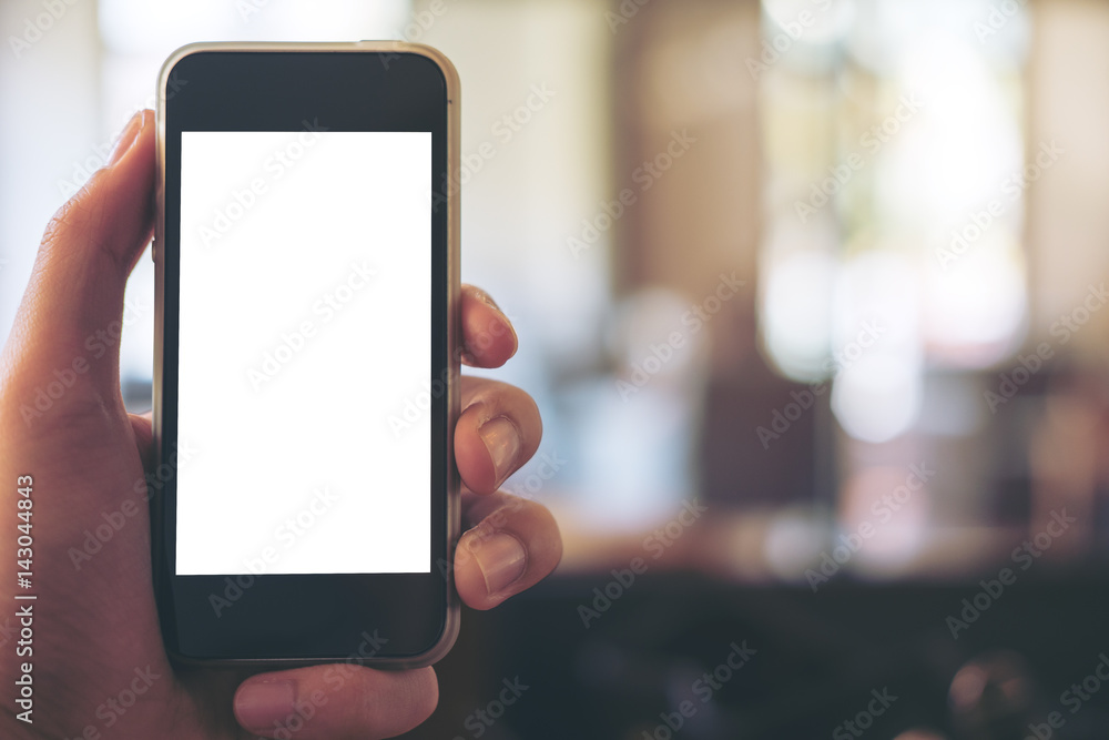 Mockup image of hand holding black mobile phone with blank white screen in vintage wooden cafe and blur bokeh background Mockup image of hand holding black mobile phone with blank white screen in vintage wooden cafe and blur bokeh background