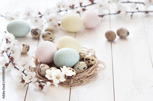 Colored chicken and quail eggs with flowers on a white wooden background. The concept of the holiday of Easter.