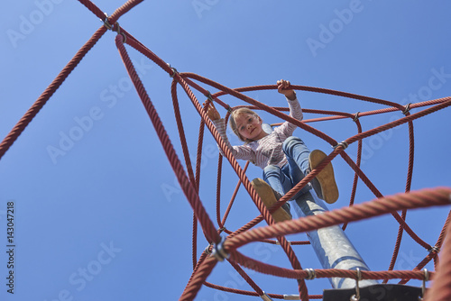 Active young child girl climbing the spider web playground activity. Children summer activities.