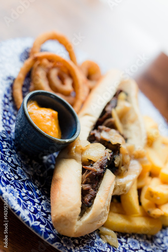 Philly Cheese Steak Sandwich mit Zwiebelringe und Pommes auf blauem Porzellan