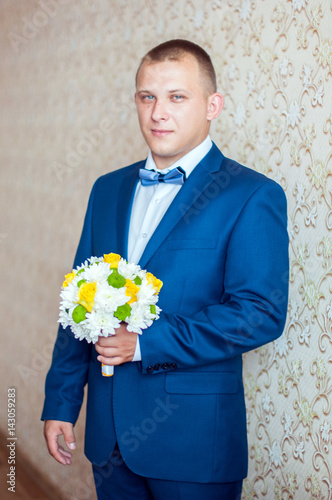Жених в синем костюме держит букет невесты из желтых роз и белых хризантем в руках. Свадьба
