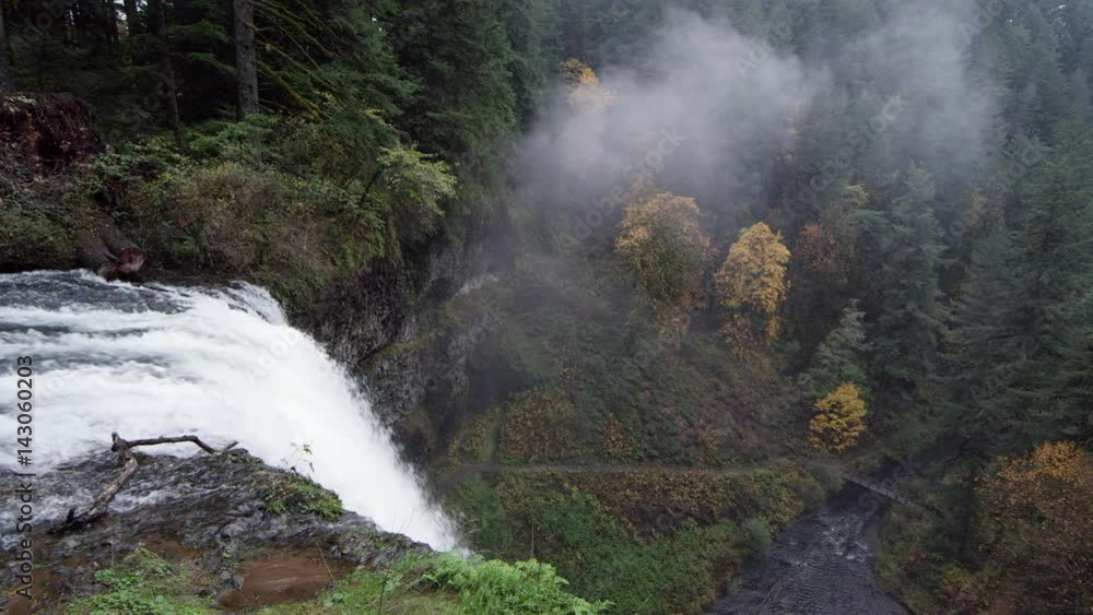 Pan over the top of the waterfall towards the forest below Pan over the top of the waterfall towards the forest below